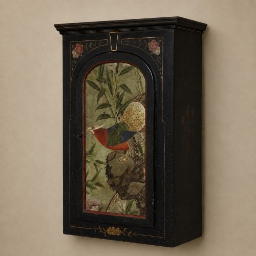 fig 5. An ebonised black wooden wall cabinet featuring an arched door panel decorated with a hand-painted exotic bird amongst green foliage.