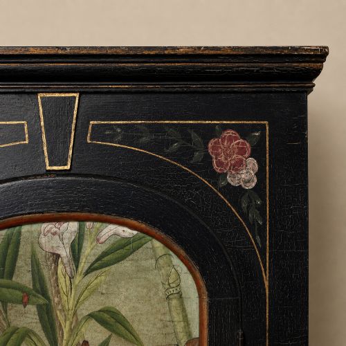 fig 7. An ebonised black wooden wall cabinet featuring an arched door panel decorated with a hand-painted exotic bird amongst green foliage.