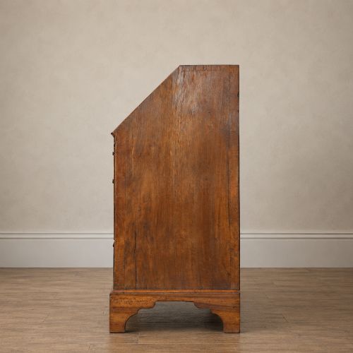 fig 5. An Early Georgian walnut bureau featuring a sloping drop-front writing lid, four graduated drawers with brass drop handles, and bracket feet.