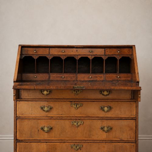 fig 7. An Early Georgian walnut bureau featuring a sloping drop-front writing lid, four graduated drawers with brass drop handles, and bracket feet.