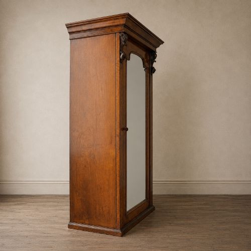 fig 2. A Victorian single-door wardrobe crafted from figured walnut wood, featuring a central arch-topped mirror panel, carved corbels, and a heavy moulded cornice.