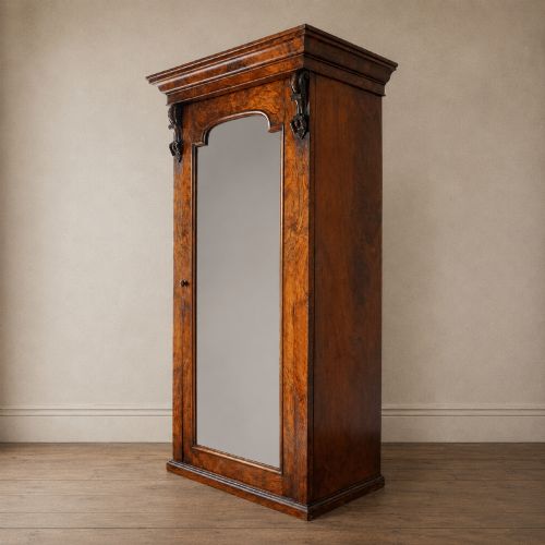 fig 3. A Victorian single-door wardrobe crafted from figured walnut wood, featuring a central arch-topped mirror panel, carved corbels, and a heavy moulded cornice.