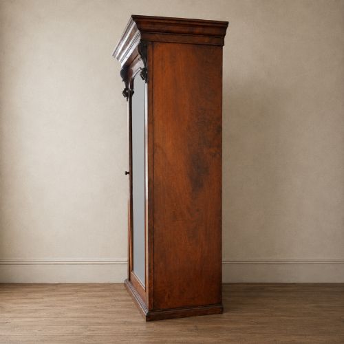 fig 4. A Victorian single-door wardrobe crafted from figured walnut wood, featuring a central arch-topped mirror panel, carved corbels, and a heavy moulded cornice.