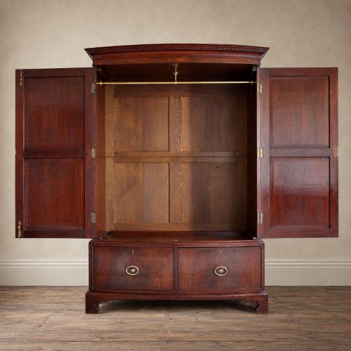 fig 1. A George III bowfront mahogany wardrobe featuring twin panelled doors with oval flame mahogany veneers above two drawers and flared bracket feet.