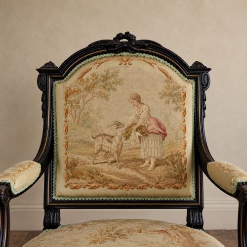 fig 6. A pair of ebonised beech Louis XVI Revival salon armchairs featuring carved frames, fluted legs, padded armrests, and tapestry upholstery, accompanied by matching footstools.