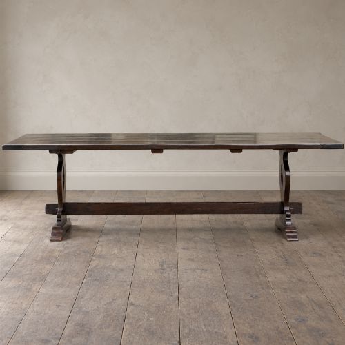 fig 1. An early twentieth-century dark oak refectory dining table featuring a plank top, pierced trestle end supports, and a central connecting stretcher.