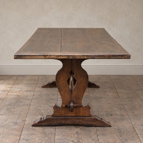 fig 3. An early twentieth-century dark oak refectory dining table featuring a plank top, pierced trestle end supports, and a central connecting stretcher.