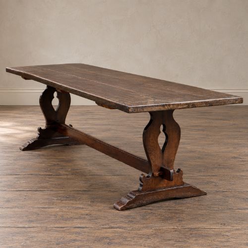 fig 4. An early twentieth-century dark oak refectory dining table featuring a plank top, pierced trestle end supports, and a central connecting stretcher.