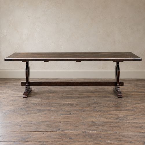 fig 5. An early twentieth-century dark oak refectory dining table featuring a plank top, pierced trestle end supports, and a central connecting stretcher.