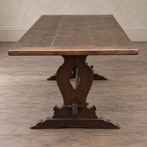 fig 6. An early twentieth-century dark oak refectory dining table featuring a plank top, pierced trestle end supports, and a central connecting stretcher.