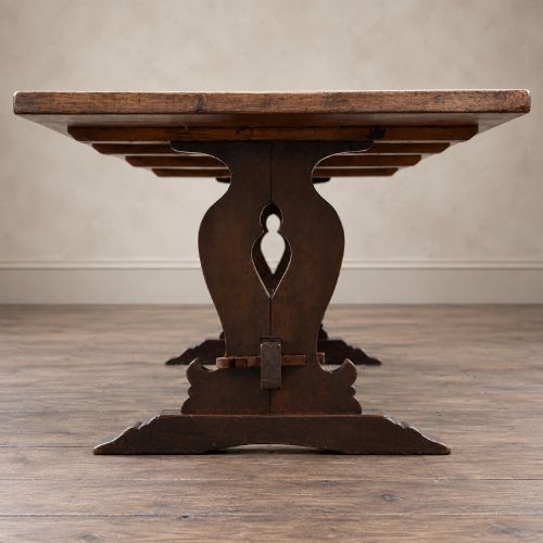 fig 9. An early twentieth-century dark oak refectory dining table featuring a plank top, pierced trestle end supports, and a central connecting stretcher.