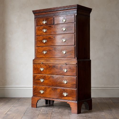 fig 1. An eighteenth-century Georgian figured mahogany chest on chest featuring a carved dentil cornice, brass swan-neck handles, a pull-out brushing slide, and bracket feet.