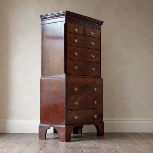 fig 5. An eighteenth-century Georgian figured mahogany chest on chest featuring a carved dentil cornice, brass swan-neck handles, a pull-out brushing slide, and bracket feet.