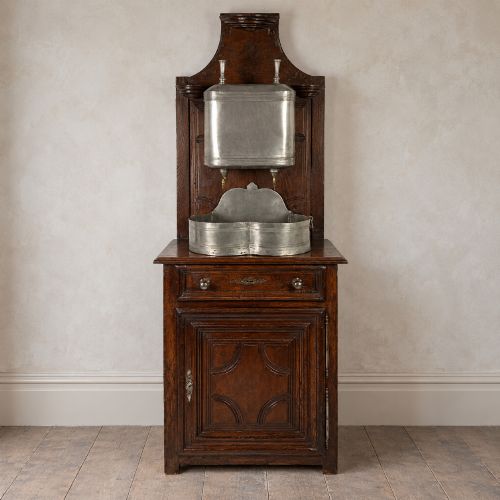 fig 2. An 18th-century dark chestnut wood lavabo cabinet featuring a carved backboard mounted with a pewter cistern above a matching pewter basin.