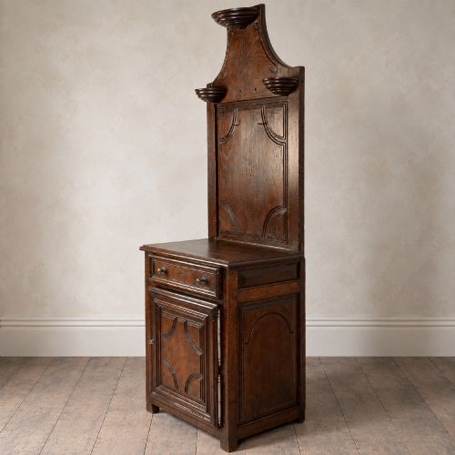 fig 6. An 18th-century dark chestnut wood lavabo cabinet featuring a carved backboard mounted with a pewter cistern above a matching pewter basin.