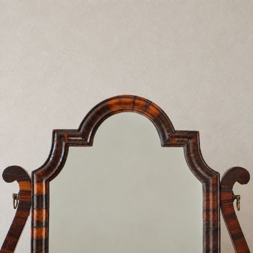 fig 4. An antique Queen Anne walnut and laburnum toilet mirror featuring an arched cross-banded frame above a serpentine base with miniature drawers.