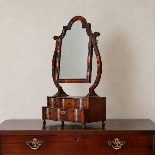 fig 5. An antique Queen Anne walnut and laburnum toilet mirror featuring an arched cross-banded frame above a serpentine base with miniature drawers.