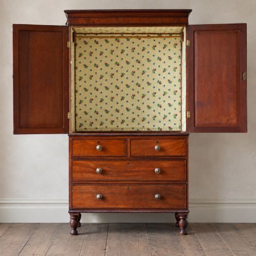 fig 1. A Regency period flame mahogany linen press featuring a two-door upper cupboard above four drawers resting on turned legs.
