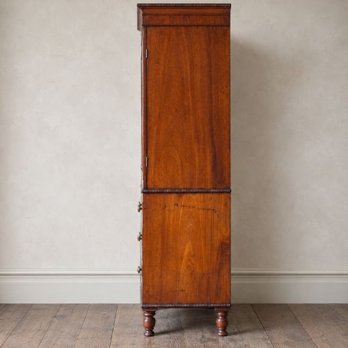 fig 3. A Regency period flame mahogany linen press featuring a two-door upper cupboard above four drawers resting on turned legs.