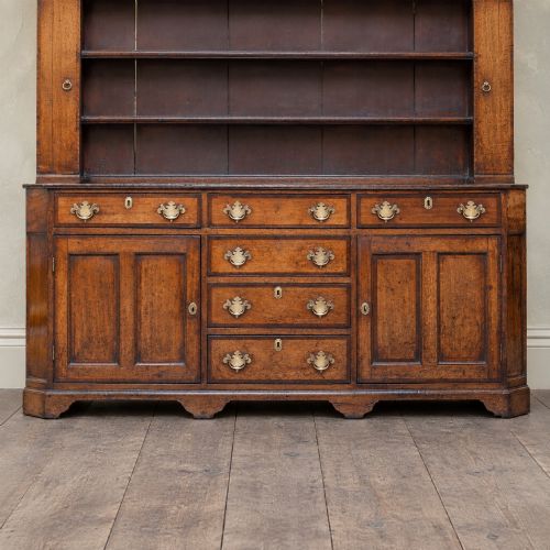 fig 1. A George II dark oak dresser with a tall open plate rack above a sideboard featuring multiple drawers and twin cupboard doors.