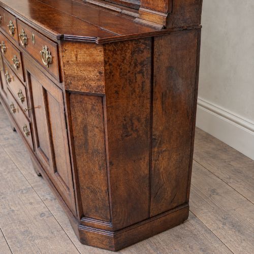 fig 3. A George II dark oak dresser with a tall open plate rack above a sideboard featuring multiple drawers and twin cupboard doors.