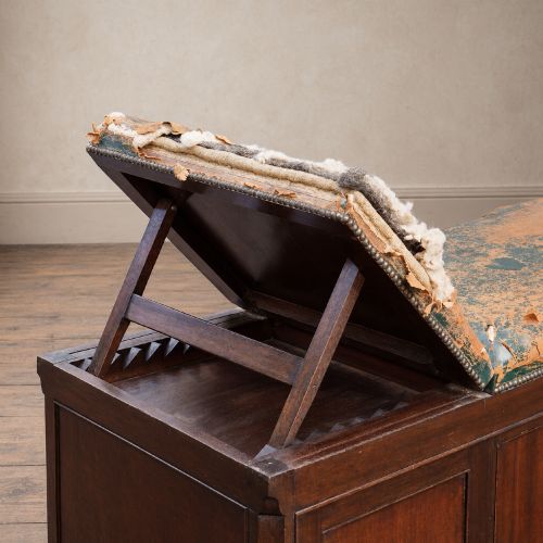 fig 5. A long antique dark mahogany bench with four panelled cupboard doors, carved ball and claw feet, and a worn leather cushion top with a raised headrest.