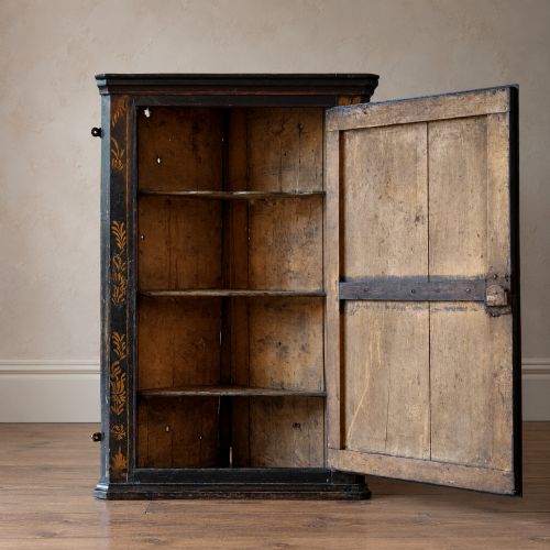 fig 1. An 18th-century black japanned single-door wall corner cupboard featuring hand-painted gold Chinoiserie figures, architectural motifs, and brass butterfly hinges.