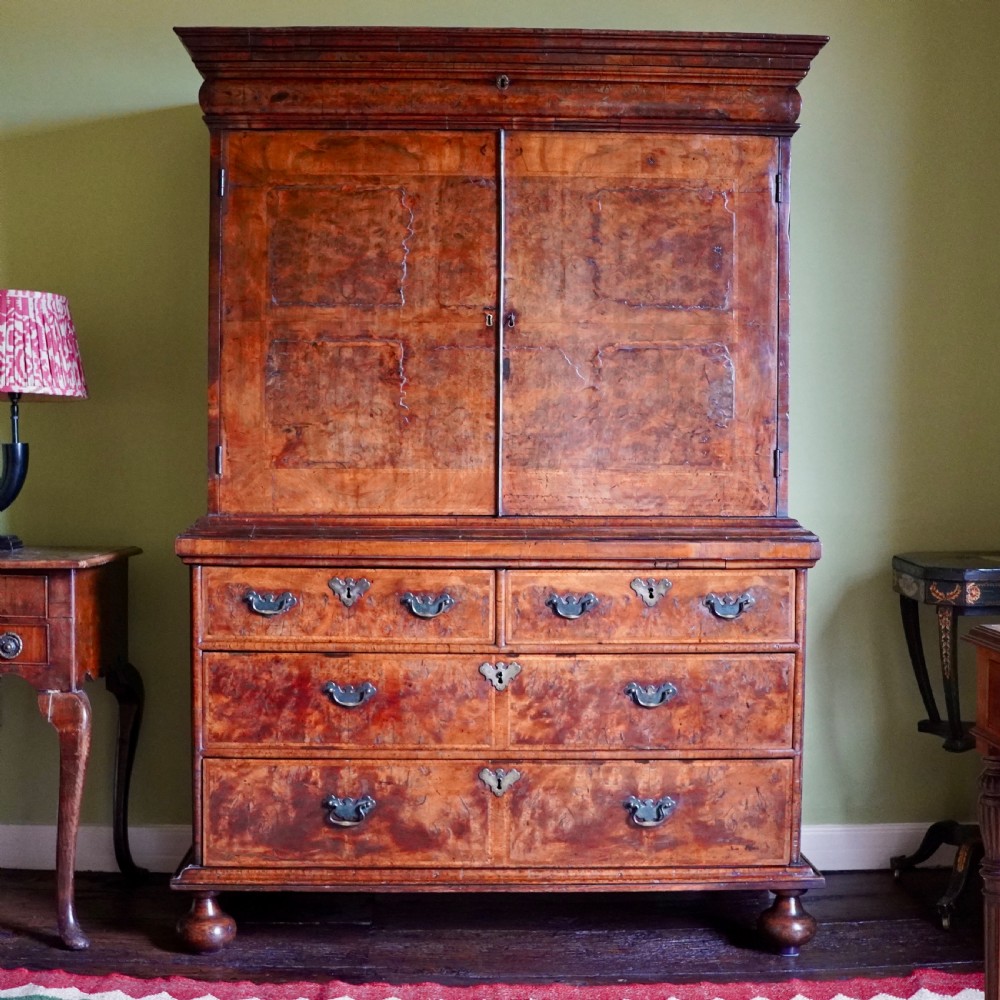 An antique Queen Anne burr walnut linen press featuring upper double cupboard doors over three lower drawers with brass handles on turned bun feet. View II