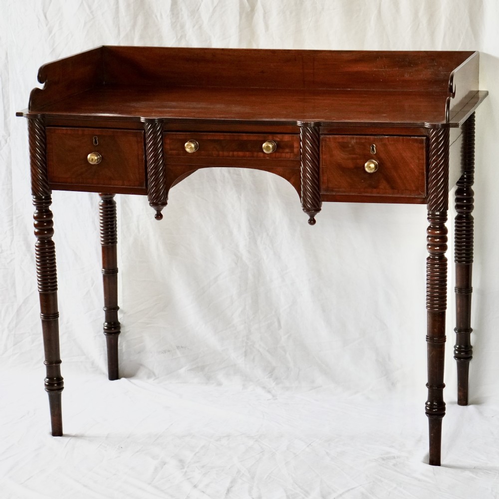 A Regency mahogany washstand featuring a gallery splashback, three drawers with brass knobs, and spiral-turned legs.