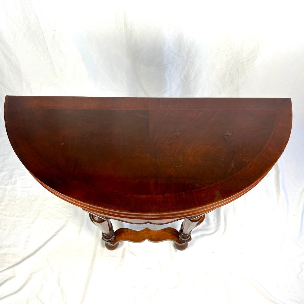 A Victorian figured walnut demi-lune card table featuring a scalloped apron, small frieze drawers, multiple turned legs, and a shaped stretcher base. View IV
