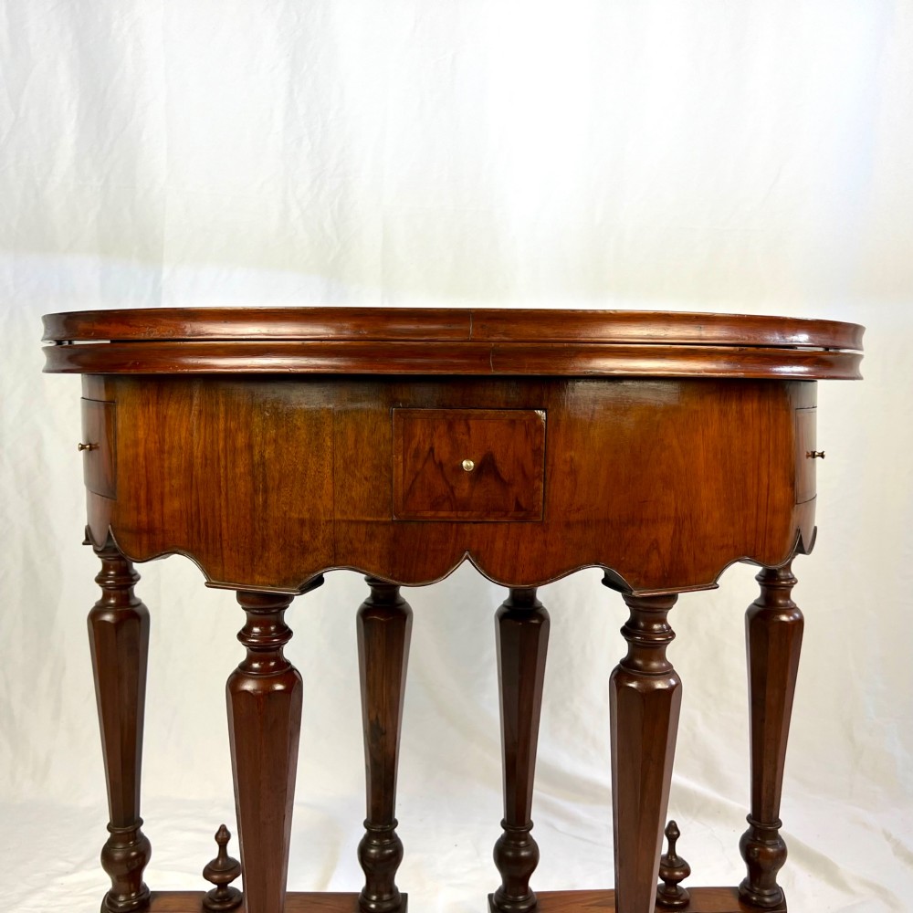 A Victorian figured walnut demi-lune card table featuring a scalloped apron, small frieze drawers, multiple turned legs, and a shaped stretcher base. View VII
