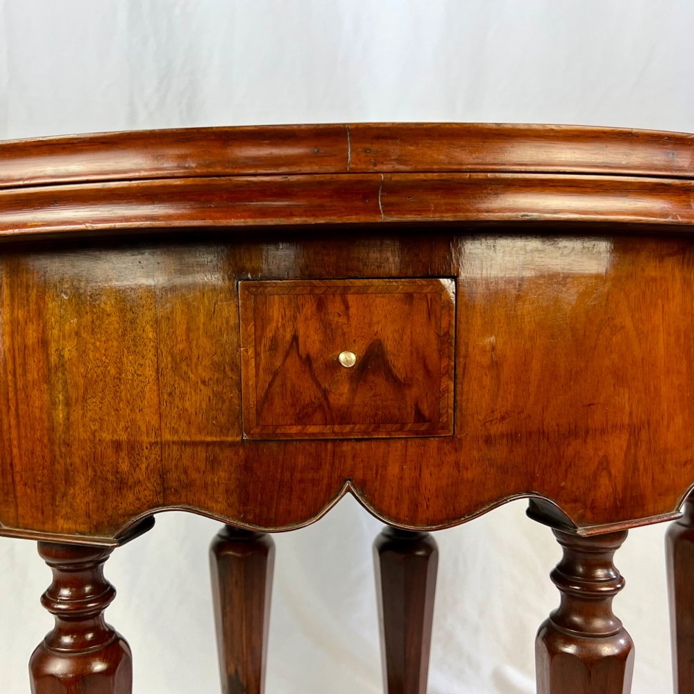 A Victorian figured walnut demi-lune card table featuring a scalloped apron, small frieze drawers, multiple turned legs, and a shaped stretcher base. View VIII