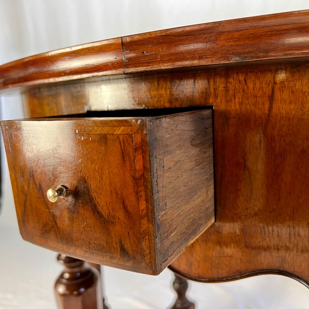 A Victorian figured walnut demi-lune card table featuring a scalloped apron, small frieze drawers, multiple turned legs, and a shaped stretcher base. View X