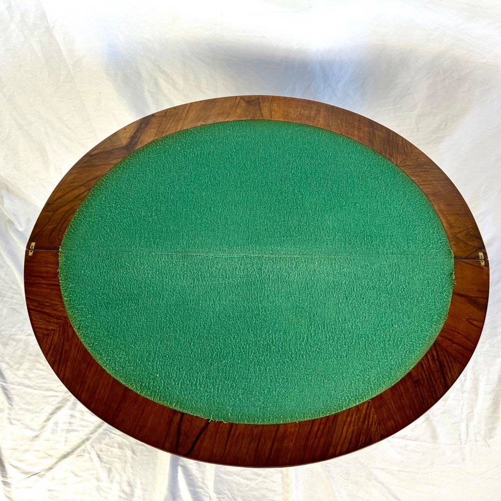 A Victorian figured walnut demi-lune card table featuring a scalloped apron, small frieze drawers, multiple turned legs, and a shaped stretcher base. View XI