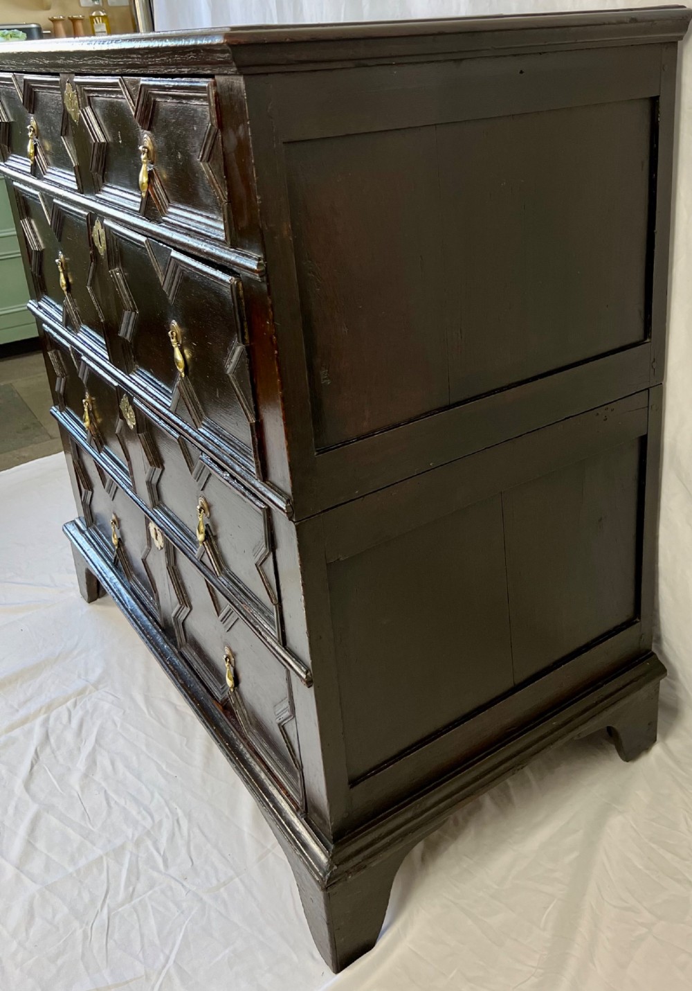 A dark oak Charles II chest of drawers featuring four geometric moulded drawer fronts with brass teardrop handles and decorative brass escutcheons. View IV