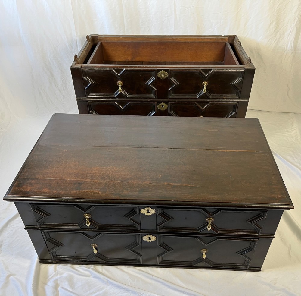 A dark oak Charles II chest of drawers featuring four geometric moulded drawer fronts with brass teardrop handles and decorative brass escutcheons. View V