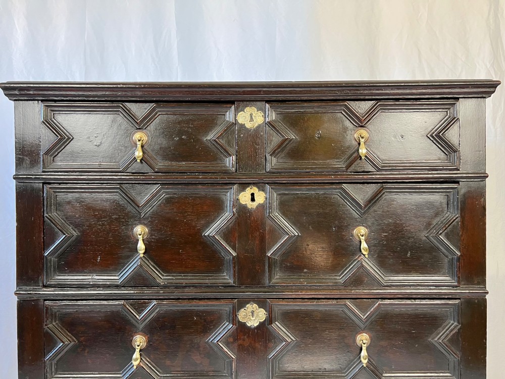 A dark oak Charles II chest of drawers featuring four geometric moulded drawer fronts with brass teardrop handles and decorative brass escutcheons. View VI