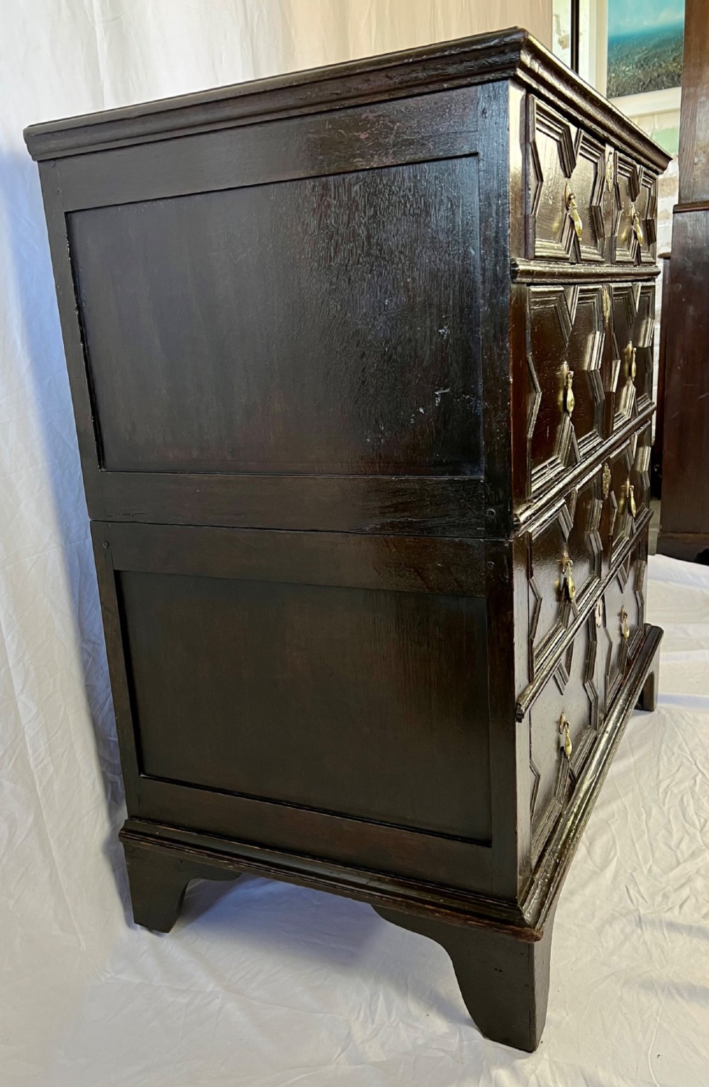A dark oak Charles II chest of drawers featuring four geometric moulded drawer fronts with brass teardrop handles and decorative brass escutcheons. View VII