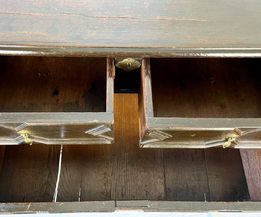 A dark oak Charles II chest of drawers featuring four geometric moulded drawer fronts with brass teardrop handles and decorative brass escutcheons. View X