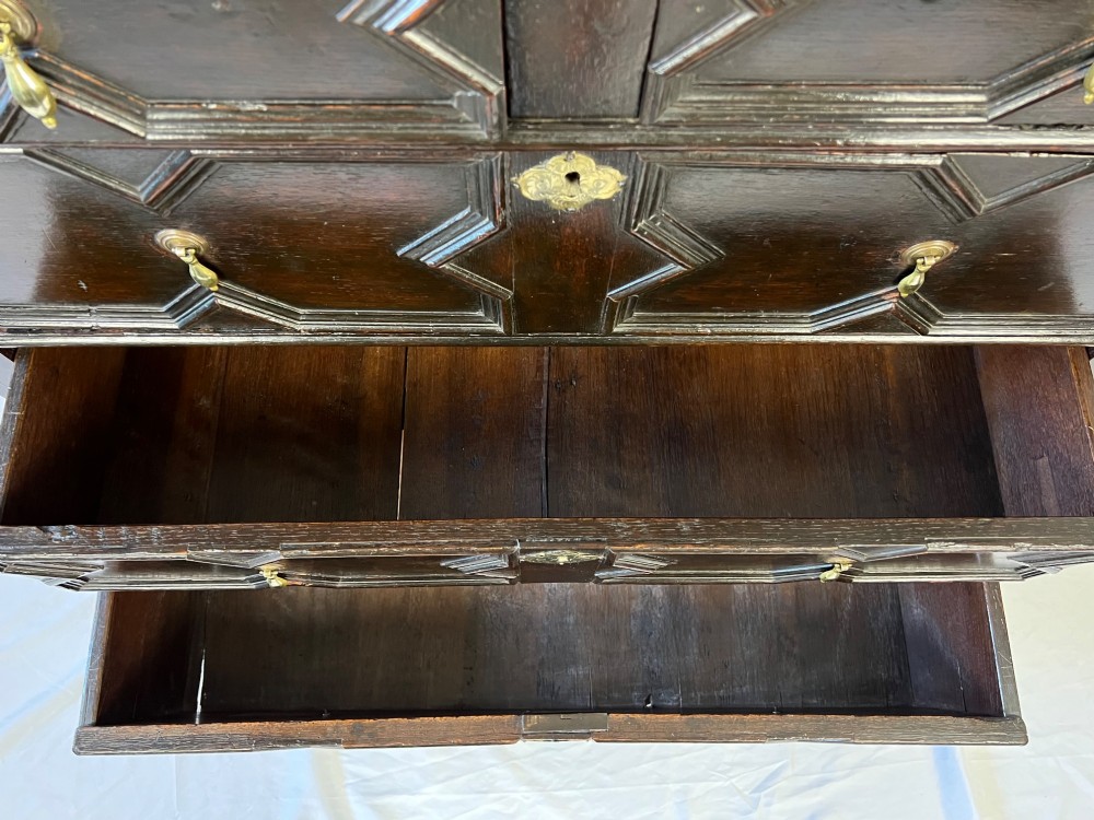 A dark oak Charles II chest of drawers featuring four geometric moulded drawer fronts with brass teardrop handles and decorative brass escutcheons. View XIII
