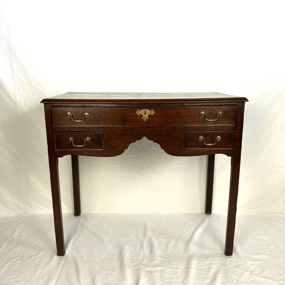 A George III dark oak lowboy table featuring three drawers with brass swan-neck handles, a shaped apron, and four square straight legs. View III