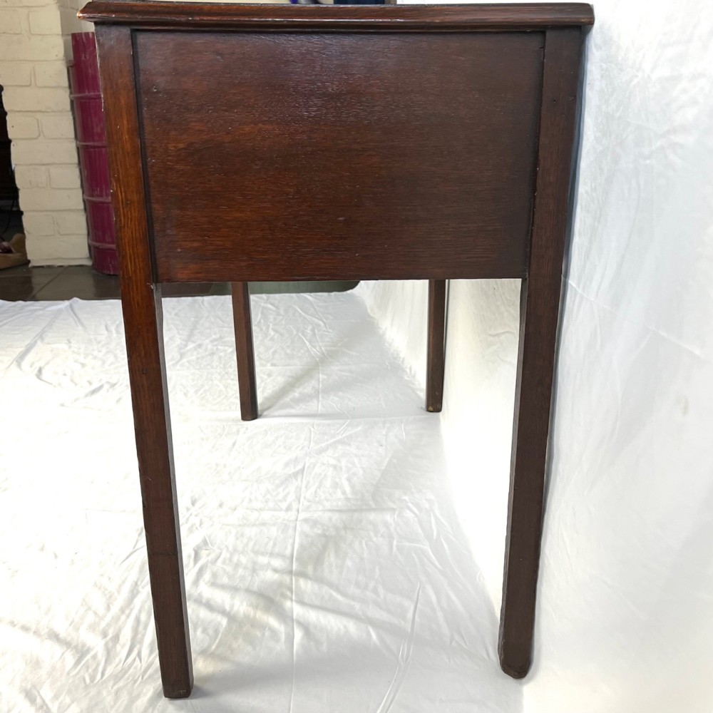 A George III dark oak lowboy table featuring three drawers with brass swan-neck handles, a shaped apron, and four square straight legs. View V