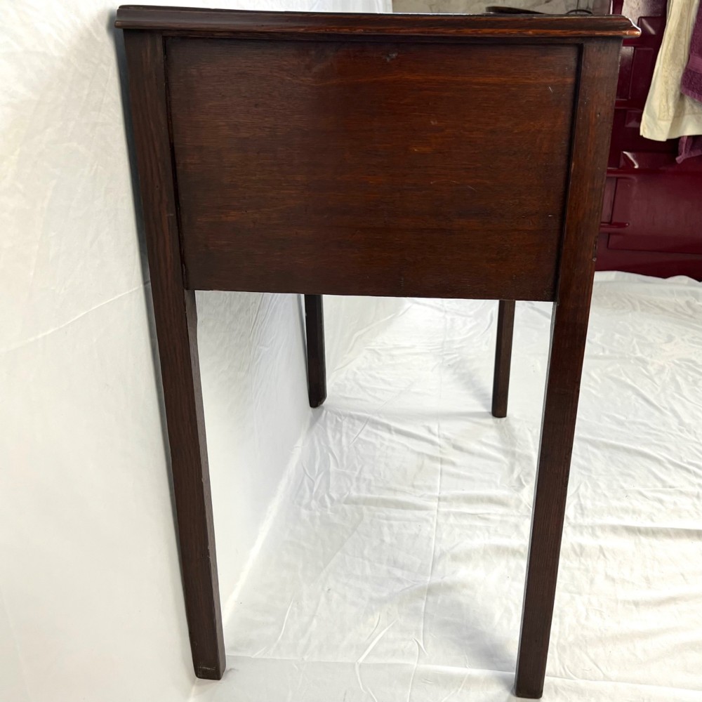 A George III dark oak lowboy table featuring three drawers with brass swan-neck handles, a shaped apron, and four square straight legs. View VI