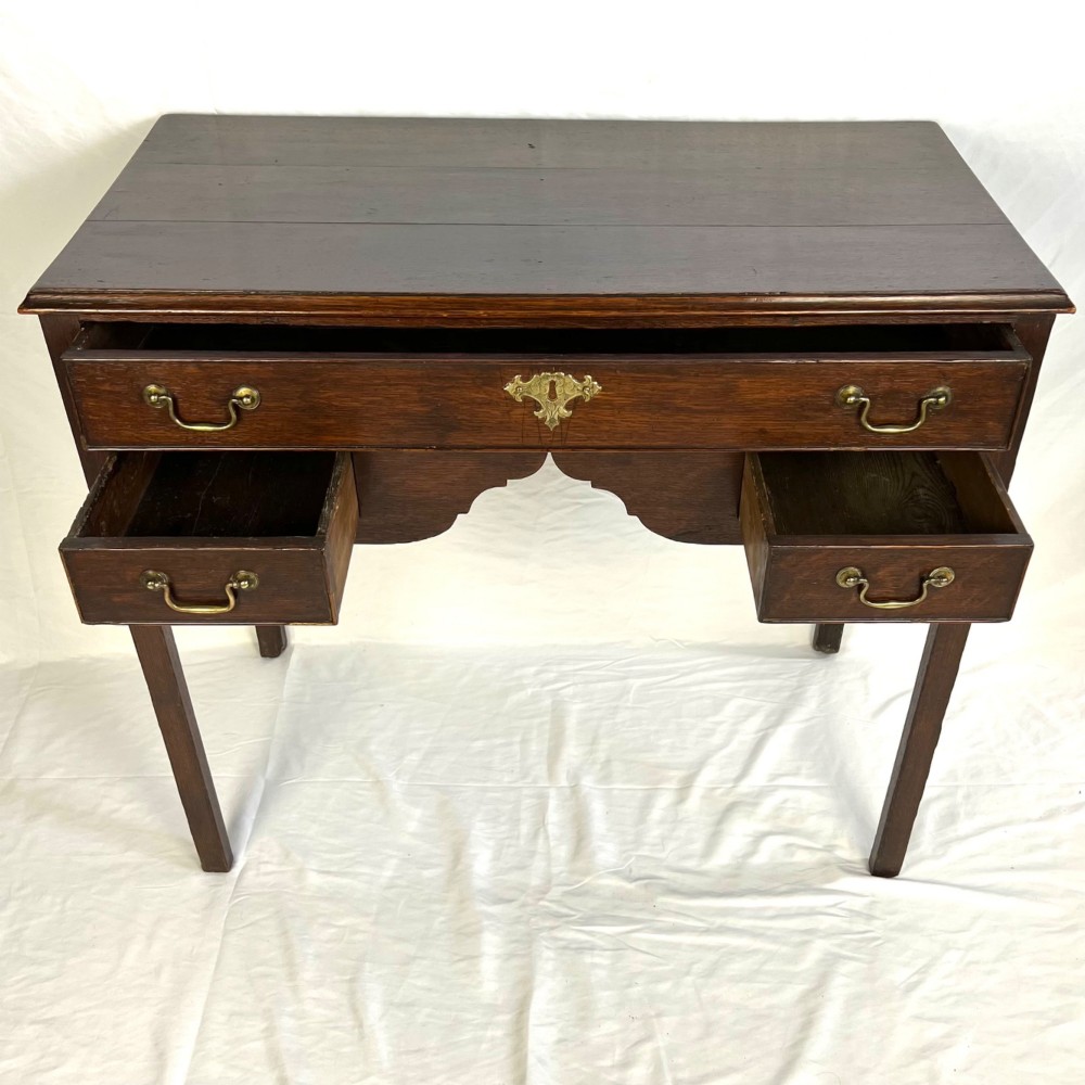 A George III dark oak lowboy table featuring three drawers with brass swan-neck handles, a shaped apron, and four square straight legs. View VII