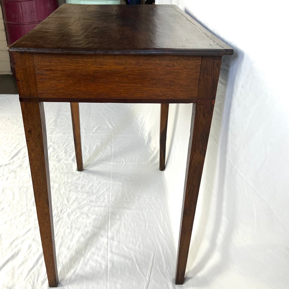 A George III dark oak lowboy table featuring three drawers with brass swan-neck handles, a shaped apron, and four square straight legs. View X