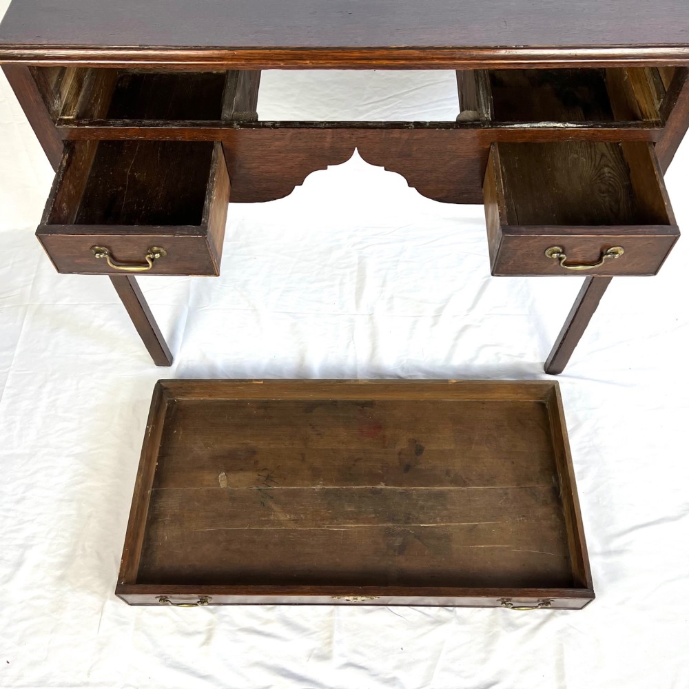 A George III dark oak lowboy table featuring three drawers with brass swan-neck handles, a shaped apron, and four square straight legs. View XIV
