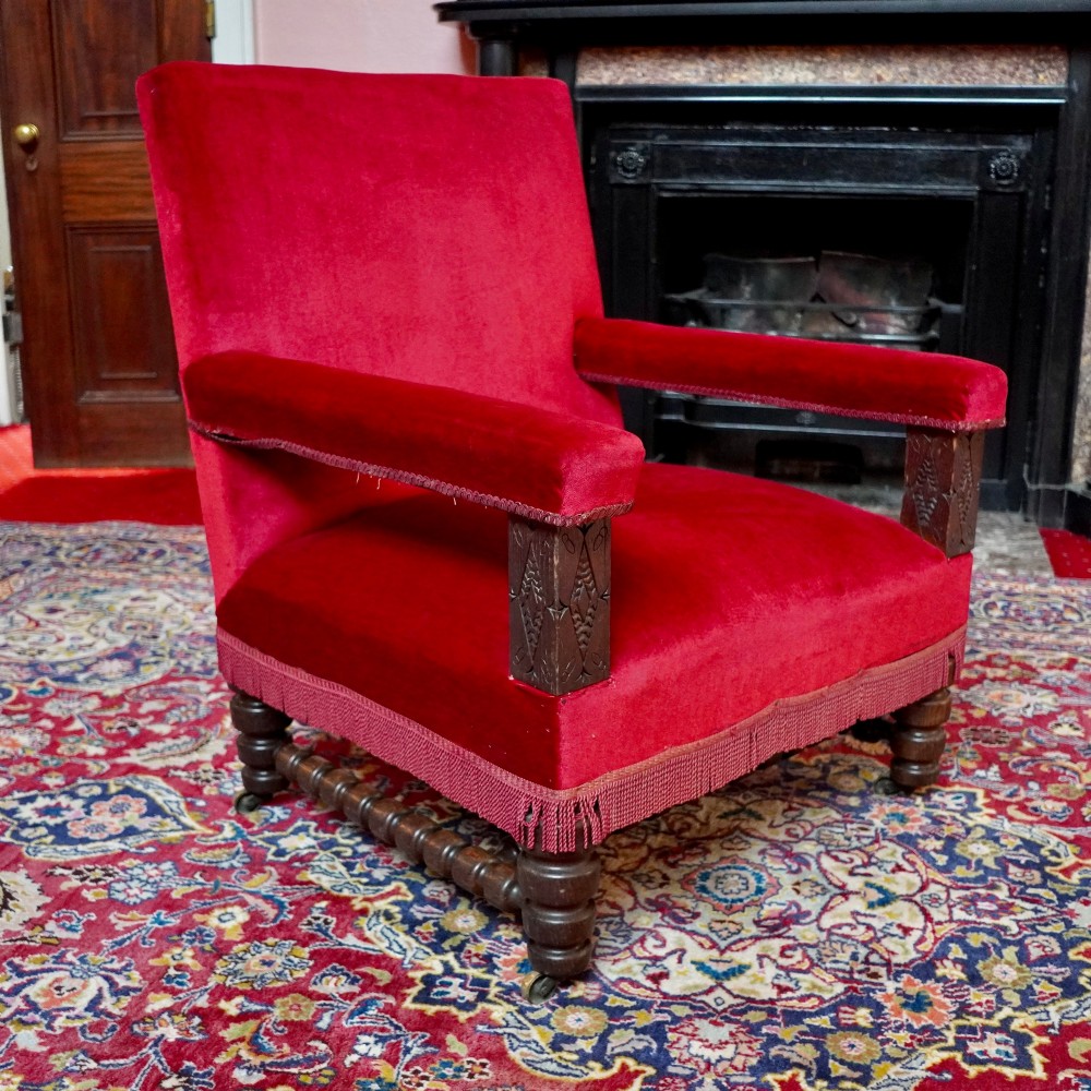 A pair of oversized Victorian armchairs upholstered in crimson red velvet with fringe trim, featuring carved oak arm supports and bobbin-turned legs. View IV