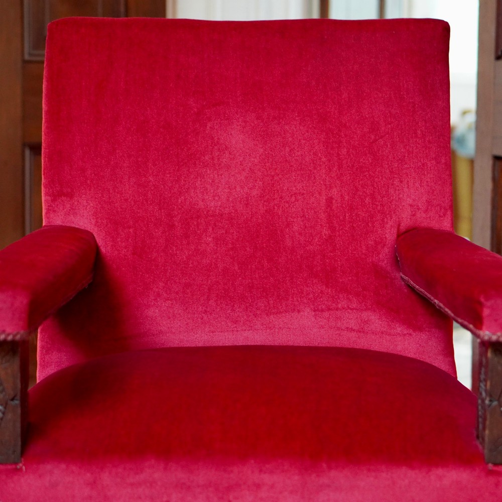 A pair of oversized Victorian armchairs upholstered in crimson red velvet with fringe trim, featuring carved oak arm supports and bobbin-turned legs. View VII