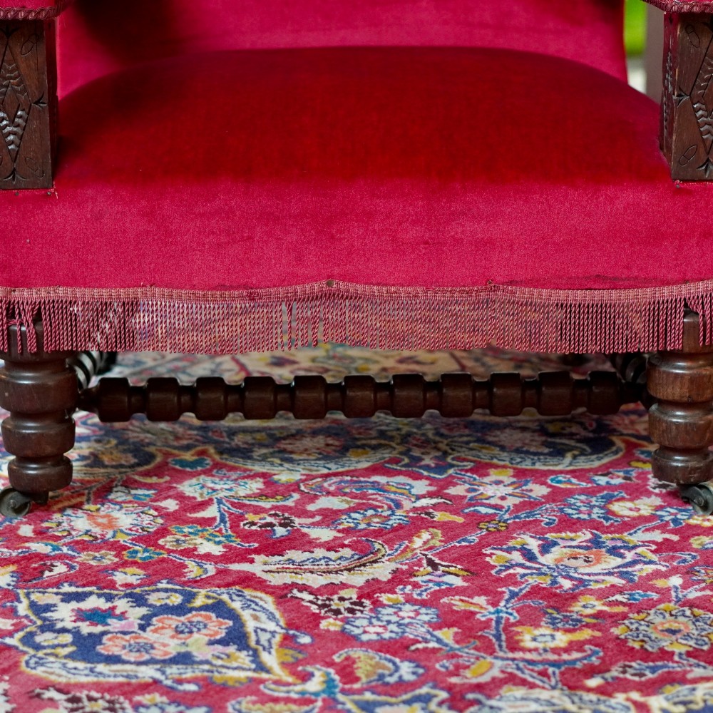 A pair of oversized Victorian armchairs upholstered in crimson red velvet with fringe trim, featuring carved oak arm supports and bobbin-turned legs. View VIII