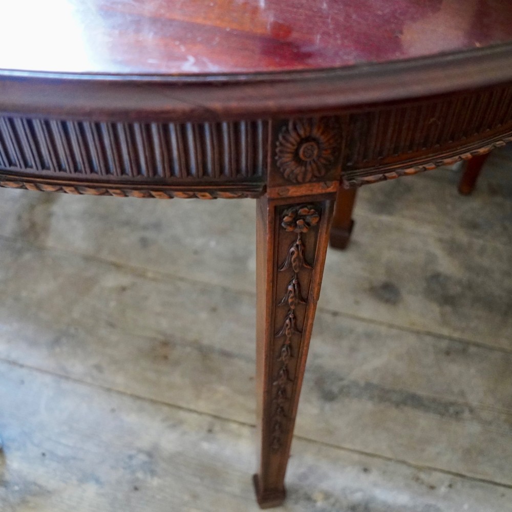 A long late George III mahogany extending dining table with D-shaped end sections, fluted friezes, carved paterae, and square tapered legs. View II